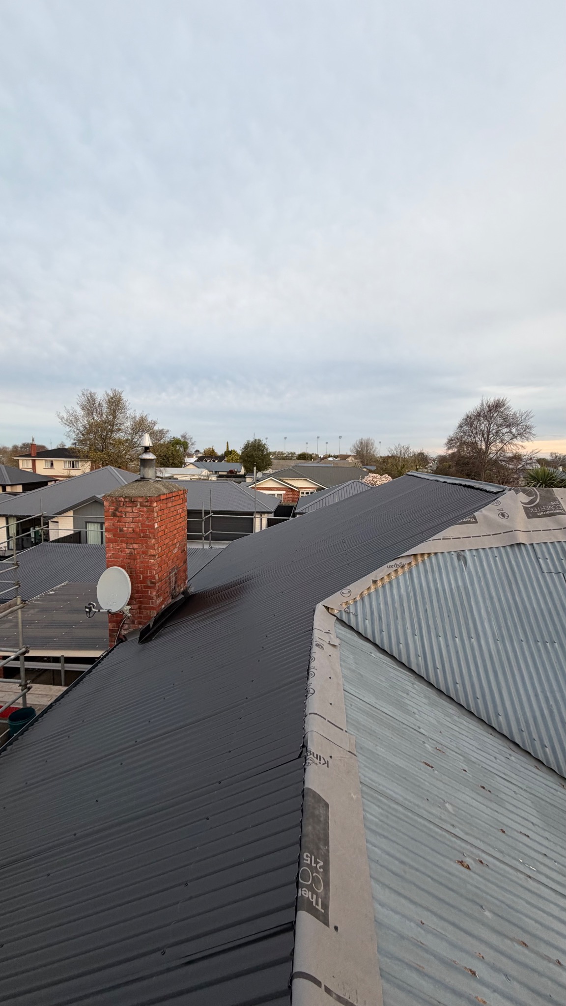 Dark metal roofing installed beside an uncovered section of roof during a reroof